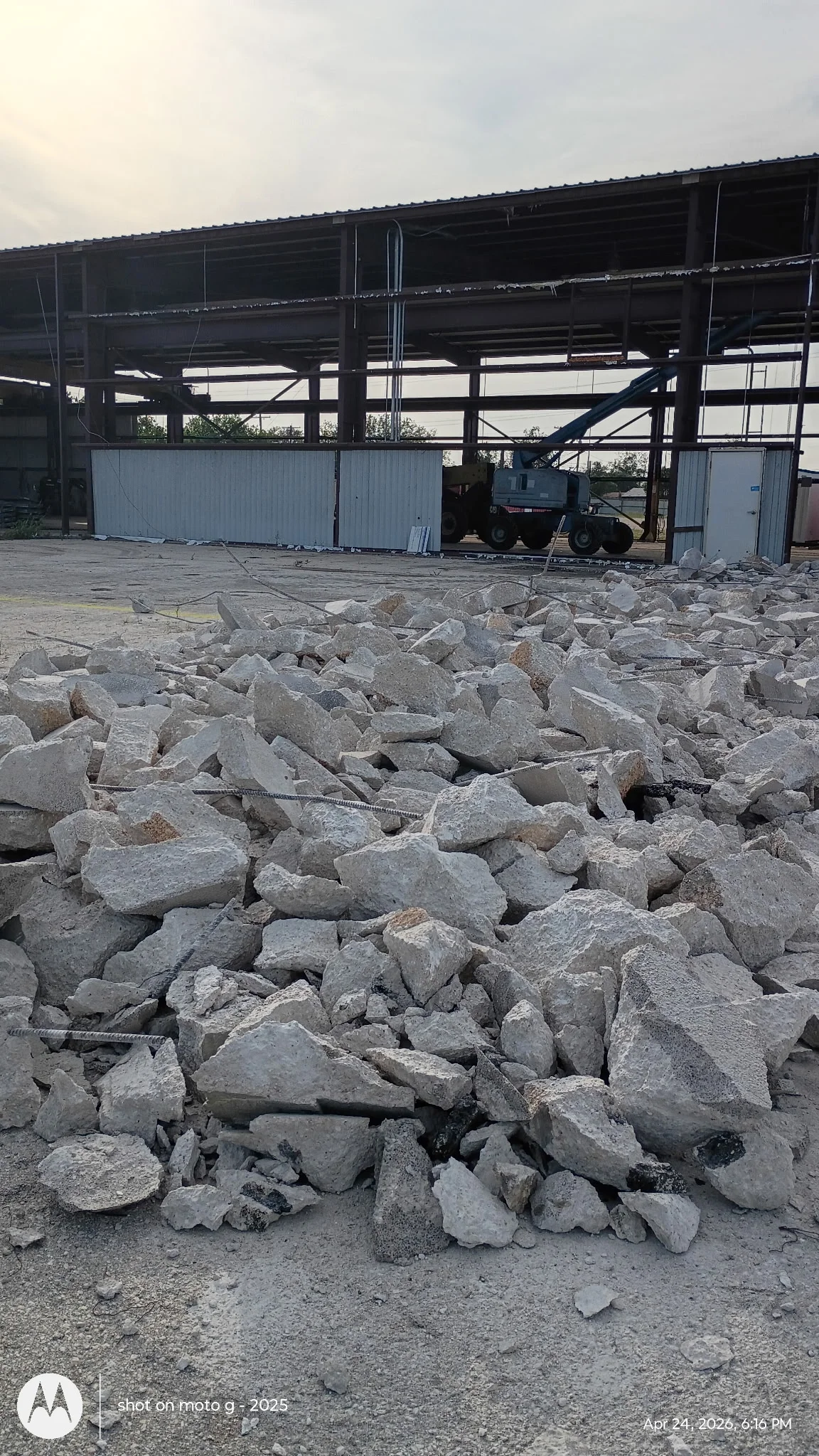 Concrete rubble pile with steel industrial structure and equipment in background