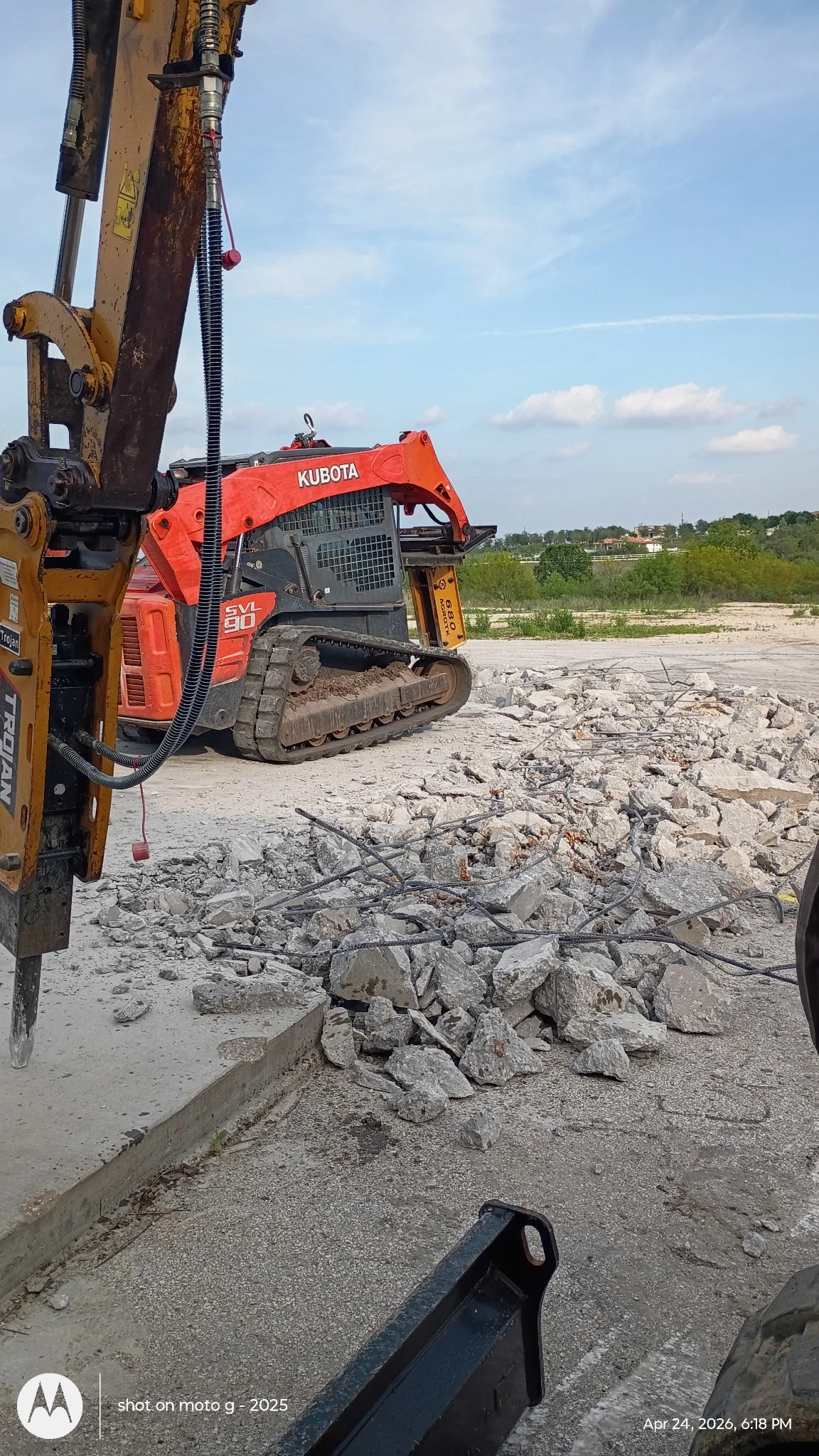 Kubota skid steer with hydraulic breaker demolishing concrete sections on open site