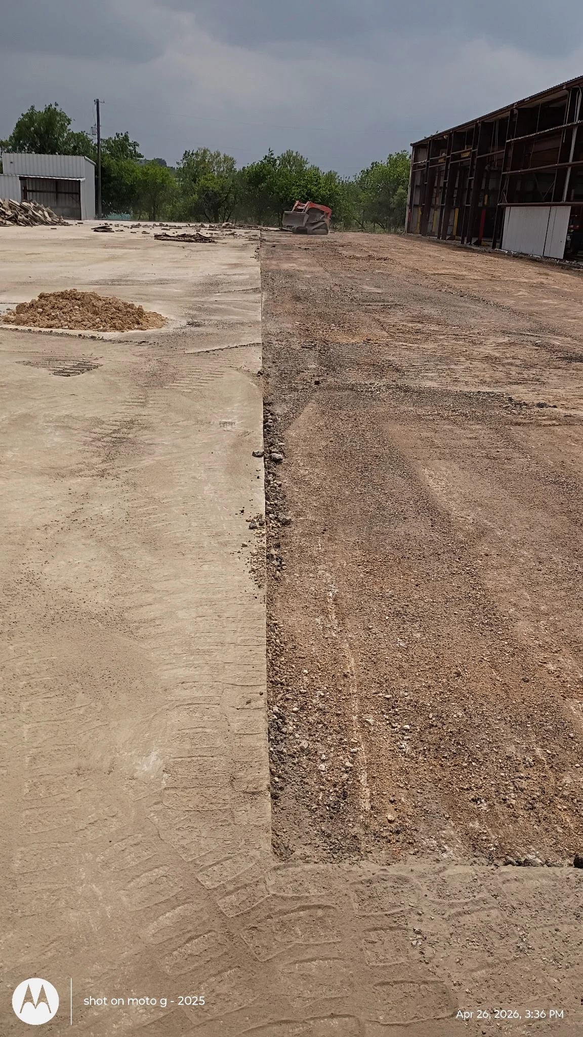 Concrete demolition and gravel base preparation on industrial site with metal buildings